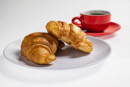 Freshly baked croissants on a plate with a cup of coffee on a white backgroundの写真素材