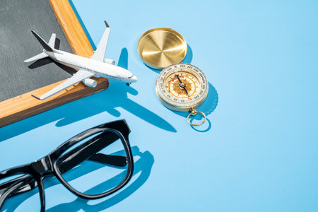 Small chalkboard, airplane, compass, and sunglasses on a blue background. Travel adventure, navigation, and planning. Concept for travel, tourism, or vacationの写真素材