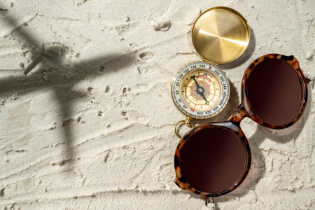 Compass and sunglasses with the shadow of an airplane flying over a beautiful sandy beach. Natural...