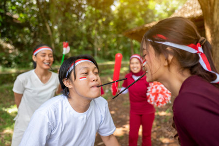 Portrait of an Indonesian southeast asian people celebrate Indonesia Independence Day on the 17th of August with a game of moving the rubber band with a straw outdoors. Concept of Kemerdekaan Indonesiaの写真素材
