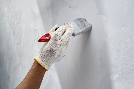 Construction worker in gloves using a paintbrush to apply paint to a wall during home renovation. Home renovation projectの写真素材