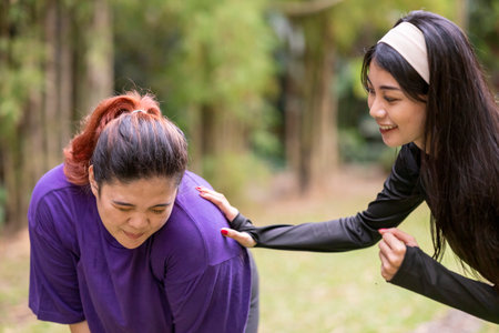 Indonesian southeast asian women in a sporty outfit encouraging her friend while running exercise in a public park outdoors. Concept of a Healthy active lifestyleの写真素材