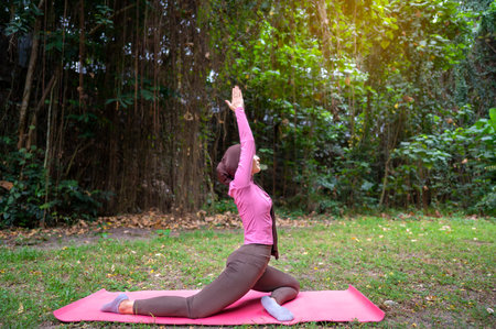 Indonesian southeast asian muslim woman in a sporty outfit practices yoga on a fitness mat in a...