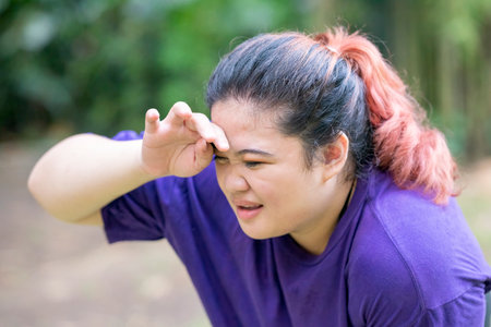 Indonesian southeast asian overweight woman in a sporty outfit tired after practice running exercise in a public park outdoors. Concept of a Healthy active lifestyle and body inclusivityの写真素材