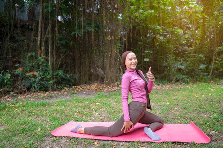 Indonesian southeast asian muslim woman in a sporty outfit practices yoga on a fitness mat in a...