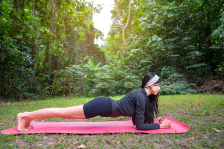Indonesian southeast asian woman in a sporty outfit practices exercise on a mat in a public park outdoors. Concept of a Healthy active lifestyleの写真素材