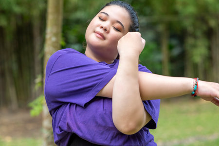 Indonesian southeast asian overweight woman in a sporty outfit practices exercise in a public park outdoors. Concept of a Healthy active lifestyle and body inclusivityの写真素材