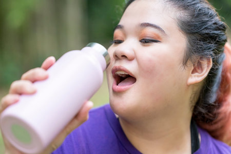Indonesian southeast asian overweight woman in a sporty outfit drinking water after practice running...