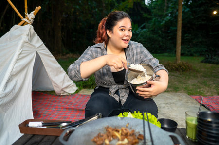 Southeast asian woman holding a metal container filled with cooked rice while camping. The scene of the lifestyle of enjoying food in a natural settingの写真素材