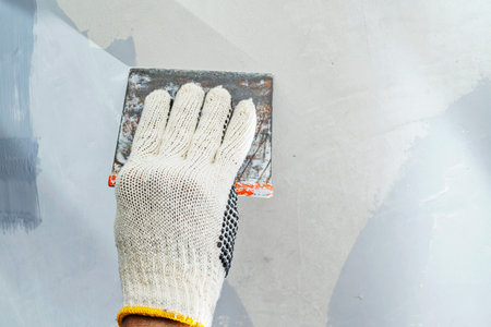 Construction worker in gloves using a scraper to fill cracks and surface imperfections on the wall during home renovation. Home renovation projectの写真素材