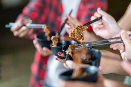 People enjoying a meal, using chopsticks to serve themselves a barbecue meal from small black bowls. The scene of the lifestyle of enjoying food in a natural settingの写真素材