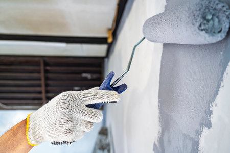 Construction worker in gloves using a paint roller to apply paint to a wall during home renovation. Home renovation projectの写真素材