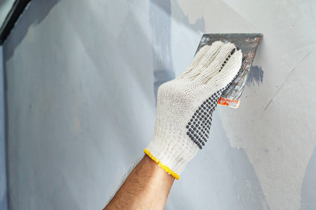 Construction worker in gloves using a scraper to fill cracks and surface imperfections on the wall during home renovation. Home renovation projectの写真素材