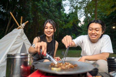 Indonesian southeast asian couple with tongs cooking sliced marinated beef bulgogi on a round grill pan with onions. The scene of the lifestyle of enjoying food in a natural settingの写真素材