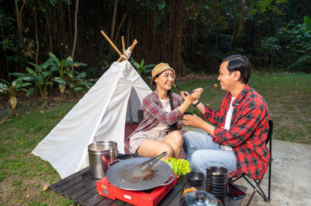 Indonesian southeast asian couple sharing food with chopsticks. Smiles and enjoying togetherness while camping outdoors. The scene of the lifestyle of enjoying food in a natural settingの写真素材