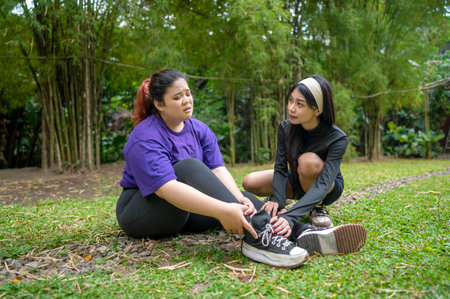 Indonesian southeast asian women in a sporty outfit help her friend with her foot after practice exercise in a public park outdoors. Concept of a Healthy active lifestyleの写真素材