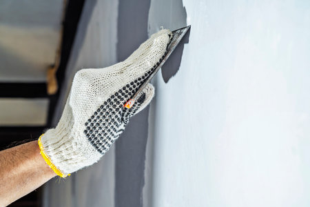 Construction worker in gloves using a scraper to fill cracks and surface imperfections on the wall during home renovation. Home renovation projectの写真素材
