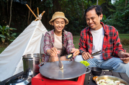 Indonesian southeast asian couple preparing for an outdoor meal, showcasing a portable stove and various ingredients. The scene of the lifestyle of enjoying food in a natural settingの写真素材