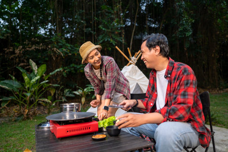 Indonesian southeast asian couple preparing for an outdoor meal, showcasing a portable stove and various ingredients. The scene of the lifestyle of enjoying food in a natural settingの写真素材