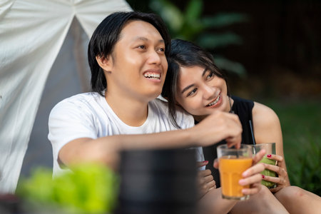 Indonesian southeast asian couple smiles while sitting together outdoors and enjoying refreshing drinks. The scene of the lifestyle of enjoying food in a natural settingの写真素材