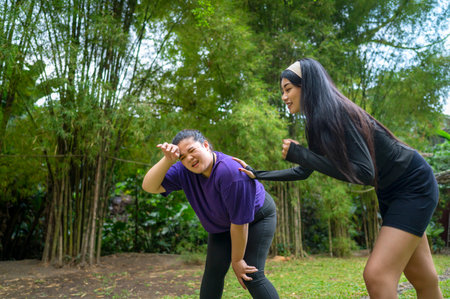 Indonesian southeast asian women in a sporty outfit encouraging her friend while running exercise in a public park outdoors. Concept of a Healthy active lifestyleの写真素材