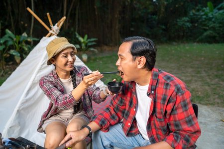 Southeast asian couple enjoying a meal with chopsticks. Smiles and enjoying togetherness while grilling and camping outdoors. The scene of the lifestyle of enjoying food in a natural settingの写真素材