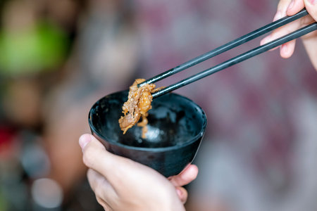 Person enjoying a meal, using chopsticks to serve themselves a barbecue meal from small black bowls. The scene of the lifestyle of enjoying food in a natural settingの写真素材
