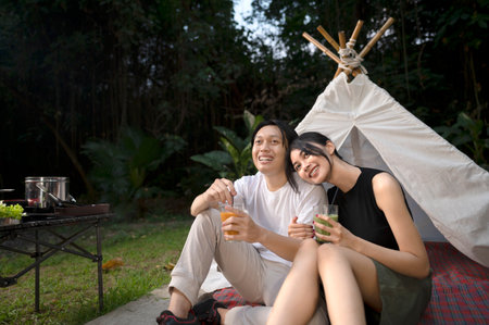 Indonesian southeast asian couple smiles while sitting together outdoors and enjoying refreshing drinks. The scene of the lifestyle of enjoying food in a natural settingの写真素材