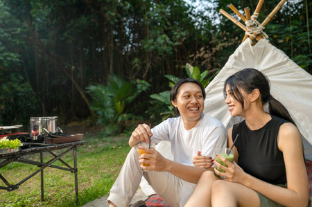 Indonesian southeast asian couple smiles while sitting together outdoors and enjoying refreshing drinks. The scene of the lifestyle of enjoying food in a natural settingの写真素材
