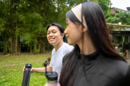 Indonesian southeast asian couple in a sporty outfit holding a drink bottle while practicing running exercise together in a public park outdoors. Concept of a Healthy active lifestyleの写真素材