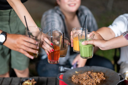 People relaxing together outdoors and enjoying refreshing drinks while cooking sliced beef on a grill pan. The scene of the lifestyle of enjoying food in a natural settingの写真素材