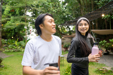 Indonesian southeast asian couple in a sporty outfit holding a drink bottle while practicing running exercise together in a public park outdoors. Concept of a Healthy active lifestyleの写真素材