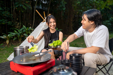 Indonesian southeast asian couple preparing for an outdoor meal, showcasing a portable stove and various ingredients. The scene of the lifestyle of enjoying food in a natural settingの写真素材