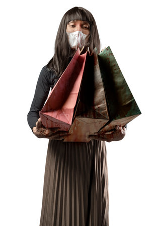 Indonesian southeast asian man dressed as a woman wearing a face mask and holding shopping bags isolated over a white background. Concept of Halloweenの写真素材