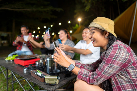 Indonesian southeast asian people enjoying a camping at night, using their cellphones to capture...