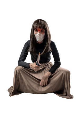 Indonesian southeast asian man dressed as a woman wearing a bloody face mask and holding a bloody knife isolated over a white background. Concept of Halloweenの写真素材