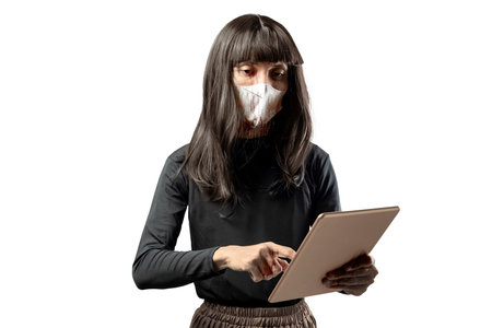 Indonesian southeast asian transgender man dressed as a woman wearing a face mask and using a tablet isolated over a white background. Concept of Halloweenの写真素材