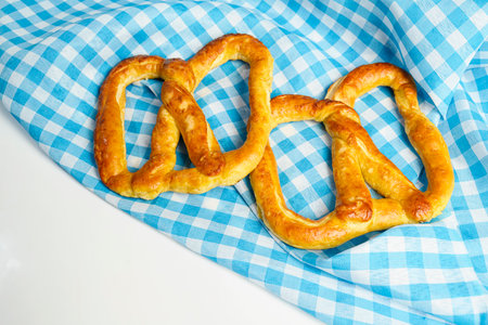 Closeup view of a pretzel loaf with a blue checkered tablecloth or napkin in a white table...