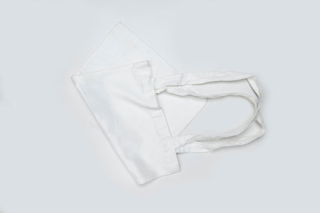 Top view of a folded eco-friendly white cotton canvas tote bag on a white background. Mockup, template, or copy space. Reusable bag for groceries and shoppingの写真素材