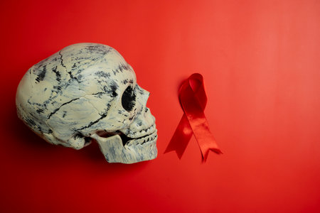 Red ribbon with a human head skull on a red background. Symbolizing awareness and support for HIV or AIDS patients. World Aids Day. Concept of Healthcare and Medicineの写真素材