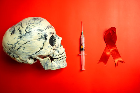 Red ribbon with a human head skull and syringe on a red background. Symbolizing awareness and...