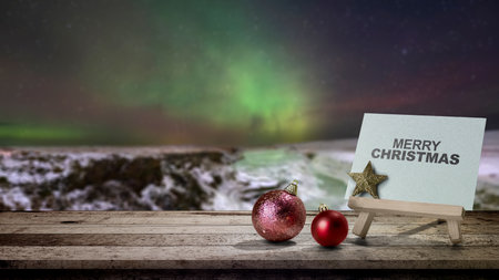 Greeting card of Merry Christmas with Christmas ornaments on the table with an Aurora Borealis background. Holiday greetings or winter themes. Concept of the Merry Christmas celebrationの写真素材