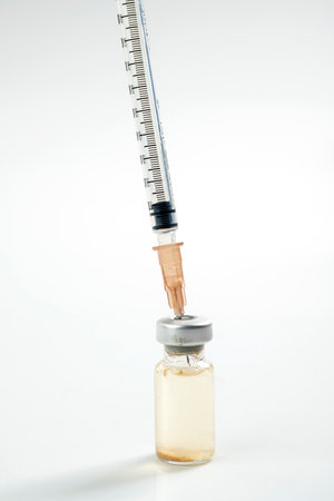 Closeup view of a disposable syringe with a needle attached, injecting a vial ready for injection vaccine on a white background. Healthcare or medicalの写真素材