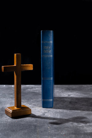 Blue book of the Holy bible and Christian cross. Standing on the table with a dark background....