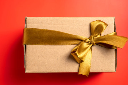 Top view of a brown gift box tied with a golden ribbon on a colored background. Mockup or copy space. Concept of decoration for holidays, anniversaries, celebrations, presents, or surprisesの写真素材