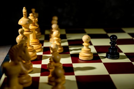Closeup view of a white chess pawn standing against the opposing pieces on the chessboard. Concept of strategyの写真素材