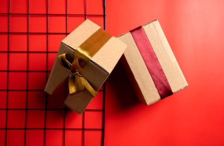 Top view of a brown gift box tied with a golden and red ribbon on a colored background. Mockup or copy space. Concept of decoration for holidays, anniversaries, celebrations, presents, or surprisesの写真素材