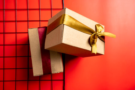 Top view of a brown gift box tied with a golden and red ribbon on a colored background. Mockup or copy space. Concept of decoration for holidays, anniversaries, celebrations, presents, or surprisesの写真素材