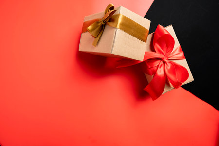 Top view of a brown gift box tied with a golden and red ribbon on a colored background. Mockup or copy space. Concept of decoration for holidays, anniversaries, celebrations, presents, or surprisesの写真素材