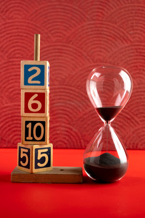 Hourglass with black sand with a wooden number block on a red background. Time passing or time...